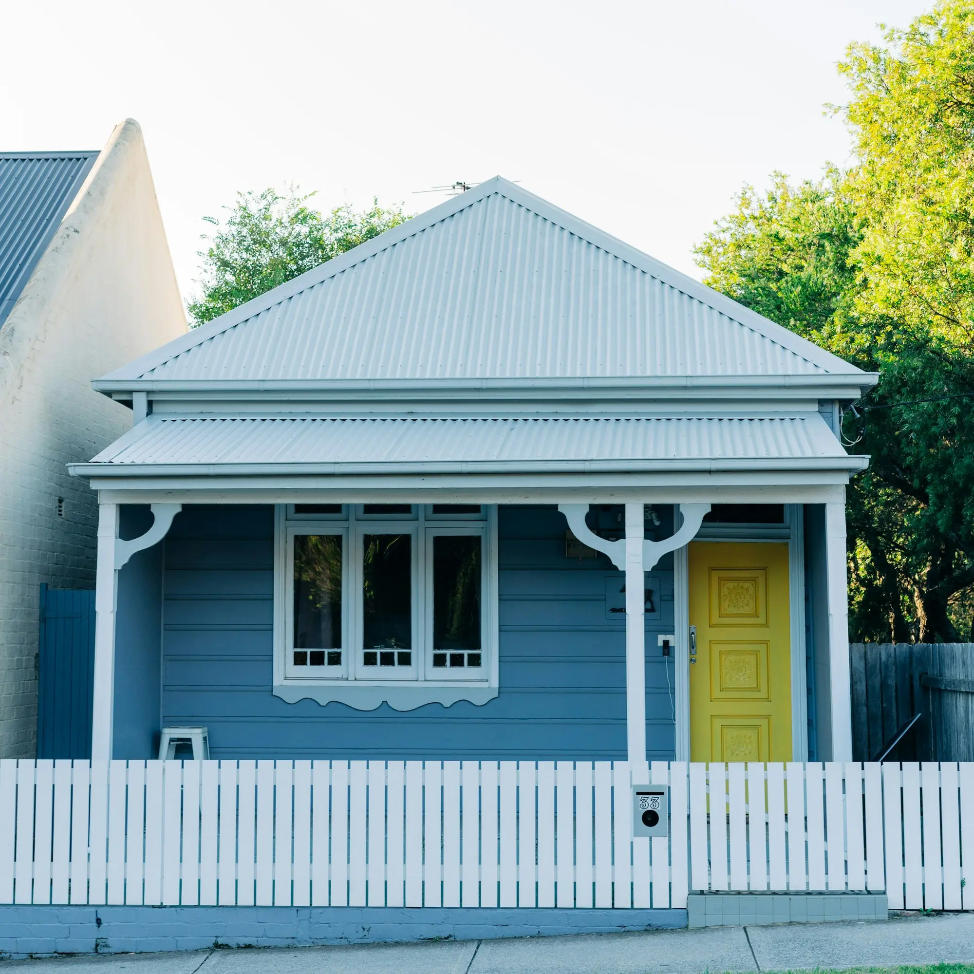 Blue weatherboard cottage with white fretwork and a yellow front door, typical of inner-suburban Victorian homes