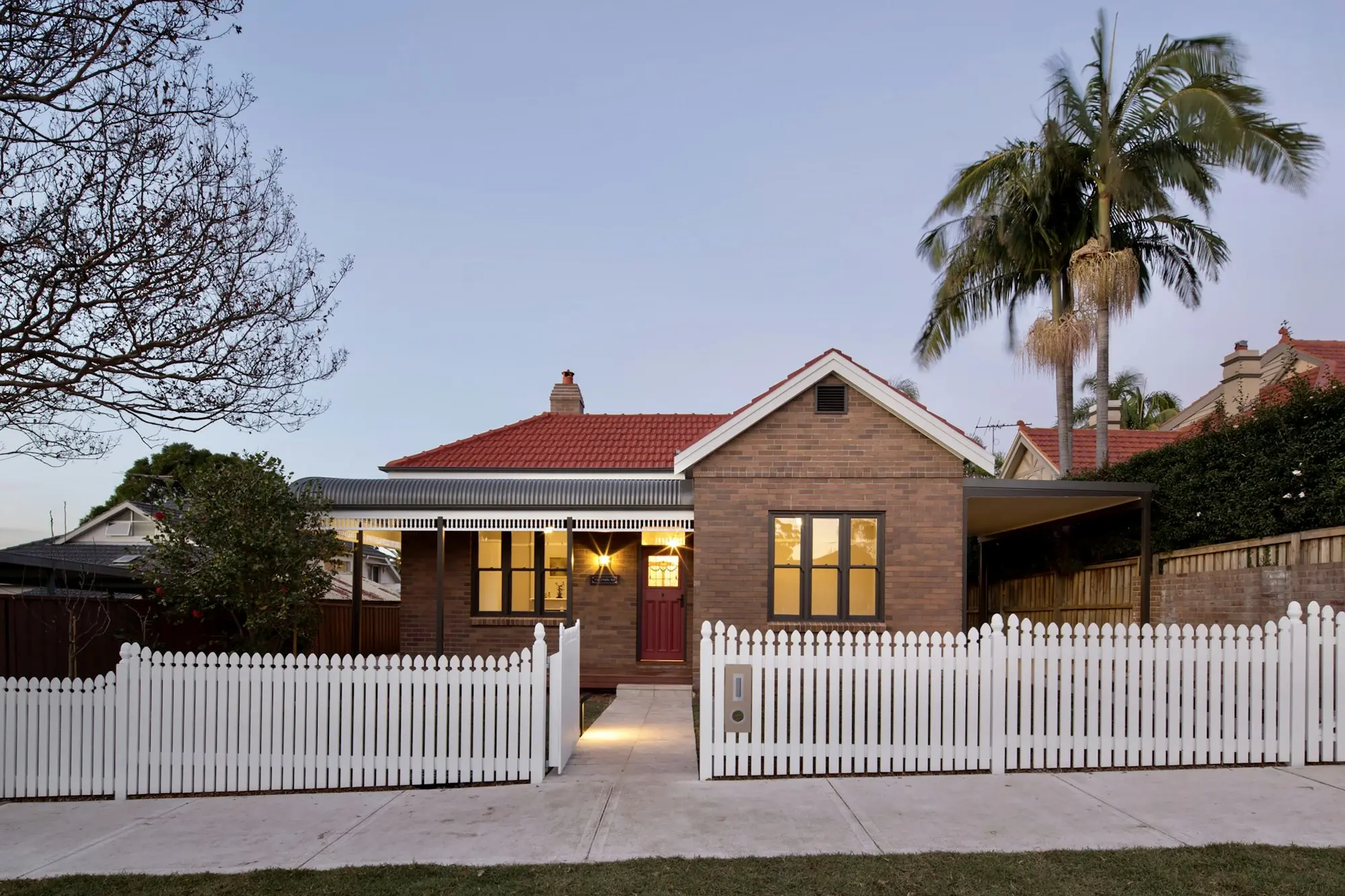 Single-storey brick family home with a white picket fence on a quiet Australian suburban street